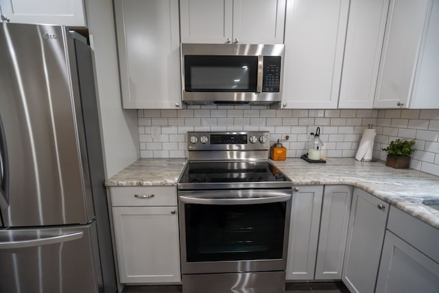 kitchen featuring stainless steel appliances, white cabinets, light stone counters, and decorative backsplash