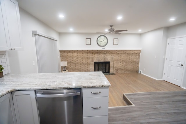 kitchen with dishwasher, white cabinets, light hardwood / wood-style floors, light stone countertops, and a brick fireplace