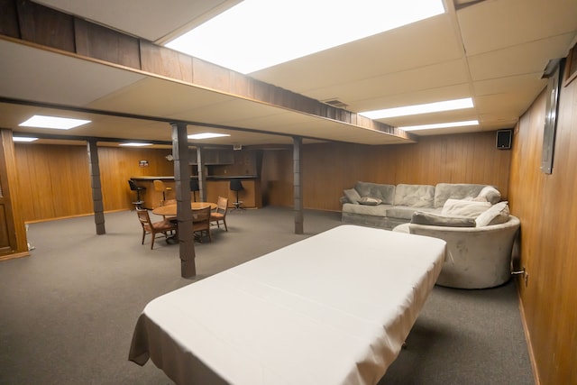 basement with a drop ceiling, carpet floors, and wood walls