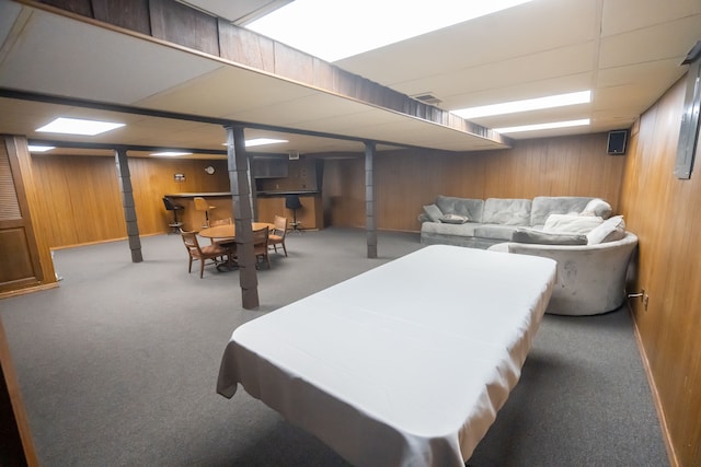 basement with a paneled ceiling, carpet, and wood walls