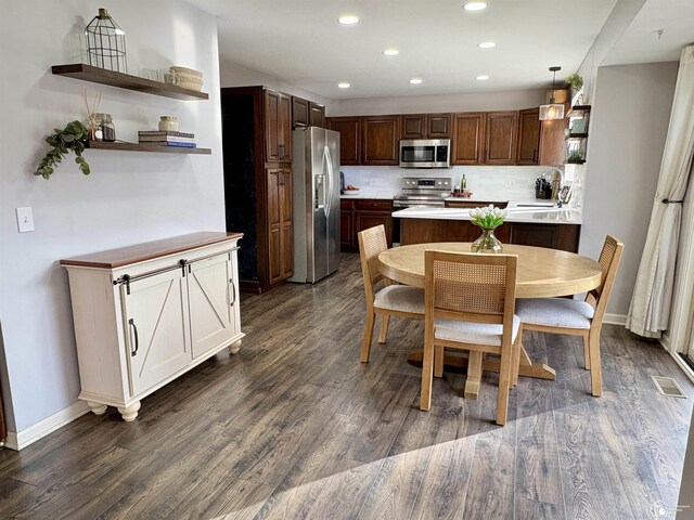 kitchen featuring appliances with stainless steel finishes, dark hardwood / wood-style floors, backsplash, hanging light fixtures, and dark brown cabinetry