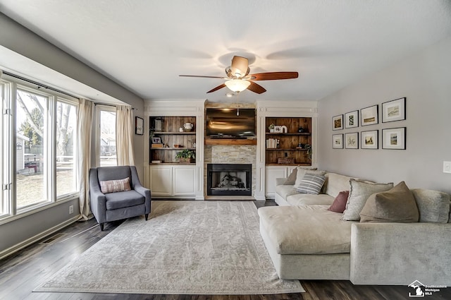 living room with a stone fireplace, dark wood-type flooring, and ceiling fan