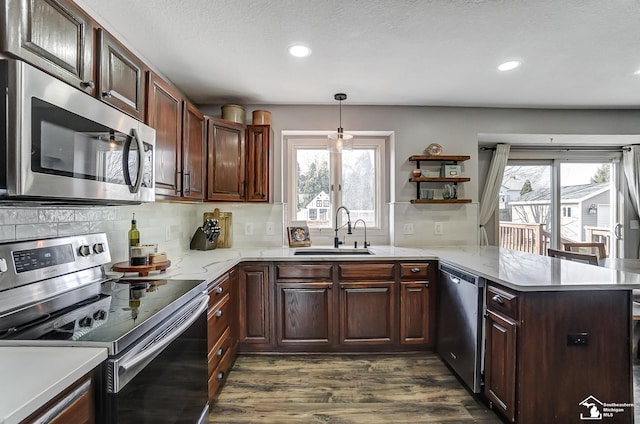 kitchen with sink, hanging light fixtures, stainless steel appliances, dark hardwood / wood-style floors, and kitchen peninsula