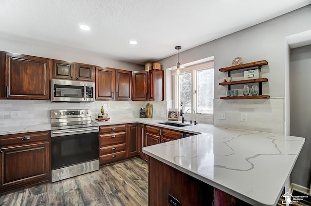 kitchen with decorative light fixtures, sink, kitchen peninsula, stainless steel appliances, and light stone countertops