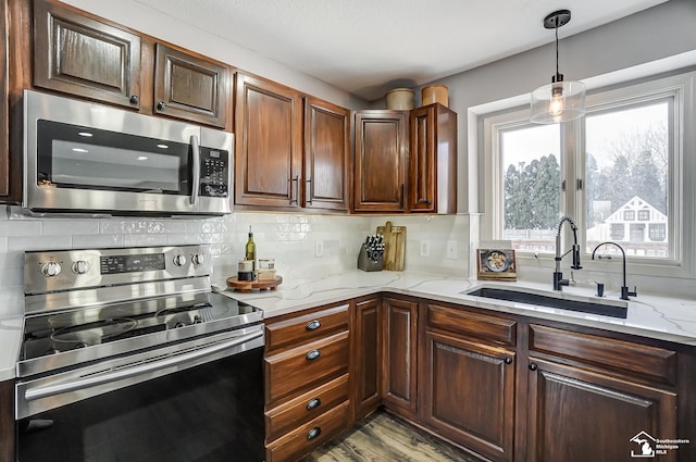 kitchen featuring sink, light stone counters, hanging light fixtures, appliances with stainless steel finishes, and backsplash