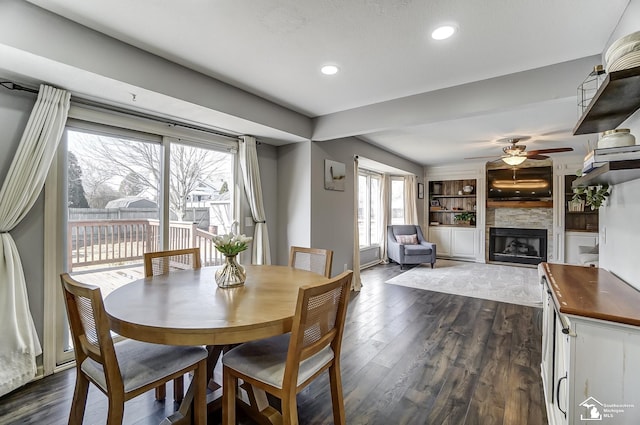 dining space featuring ceiling fan, a large fireplace, built in features, and dark hardwood / wood-style floors