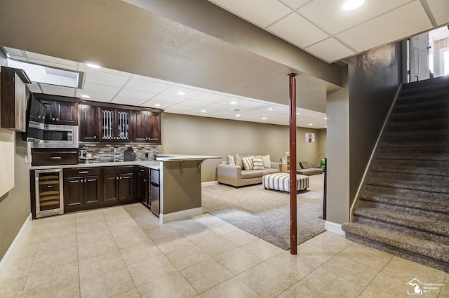 kitchen featuring dark brown cabinets, wine cooler, stainless steel microwave, tasteful backsplash, and light colored carpet