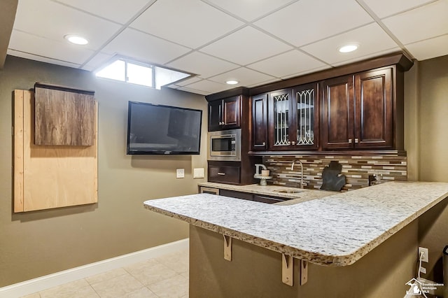 bar with sink, light tile patterned floors, dark brown cabinets, stainless steel microwave, and decorative backsplash