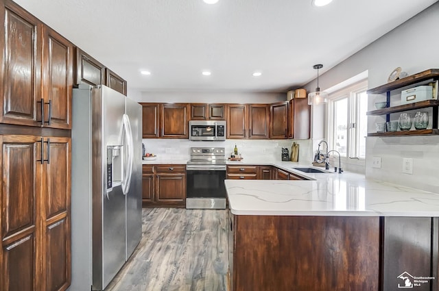 kitchen featuring sink, appliances with stainless steel finishes, kitchen peninsula, pendant lighting, and light stone countertops