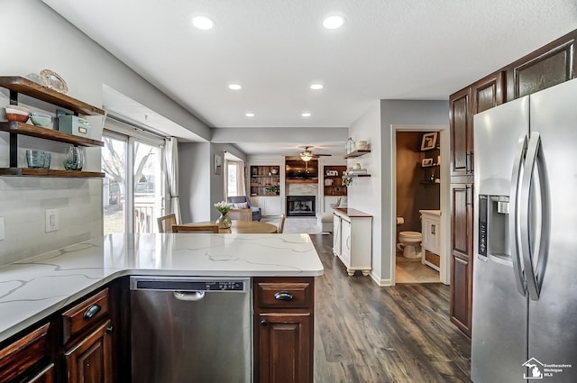 kitchen featuring dark brown cabinetry, appliances with stainless steel finishes, dark hardwood / wood-style floors, ceiling fan, and light stone countertops