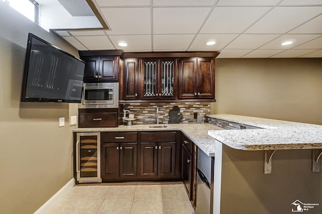 kitchen with sink, dark brown cabinets, stainless steel microwave, wine cooler, and kitchen peninsula