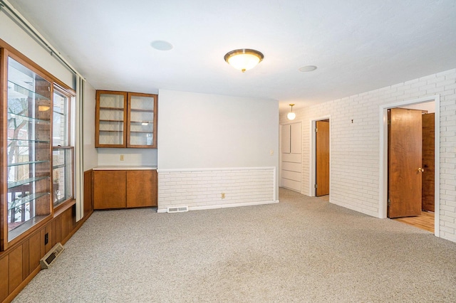 unfurnished room with brick wall and light colored carpet