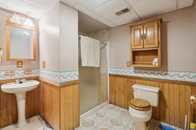 bathroom featuring a shower with shower door, wooden walls, toilet, and a paneled ceiling