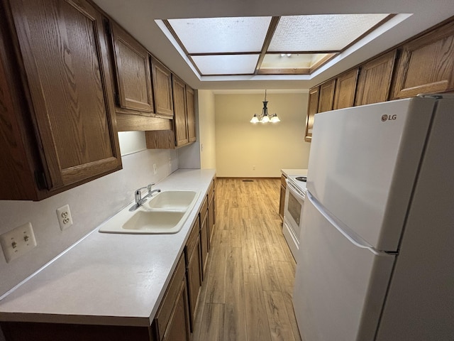 kitchen featuring pendant lighting, sink, white appliances, an inviting chandelier, and light hardwood / wood-style flooring