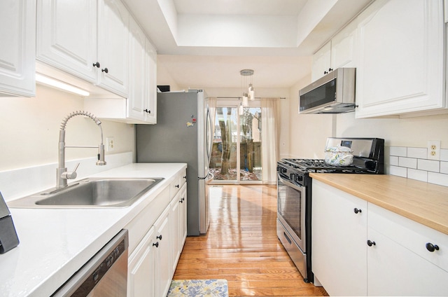 kitchen with decorative light fixtures, sink, white cabinets, stainless steel appliances, and light hardwood / wood-style flooring