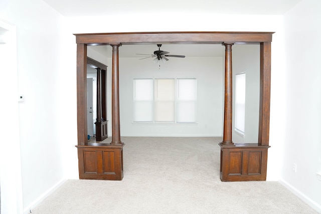 unfurnished living room featuring ceiling fan, light colored carpet, and decorative columns