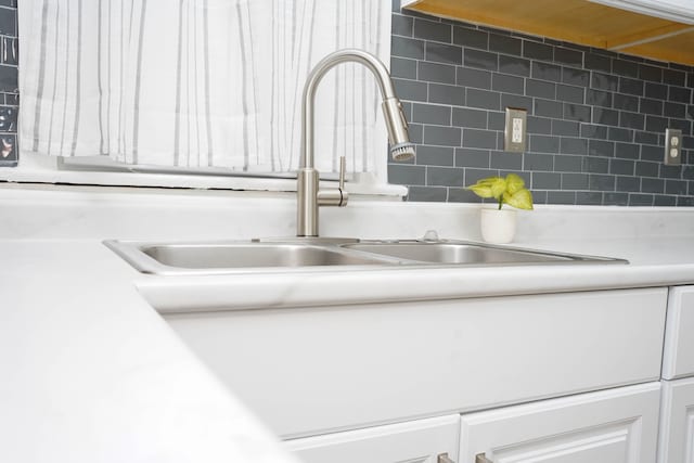 room details featuring tasteful backsplash, sink, and white cabinets