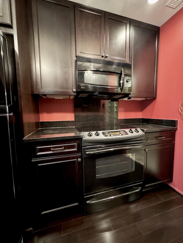 kitchen featuring dark brown cabinetry, dark stone countertops, dark hardwood / wood-style flooring, and black appliances