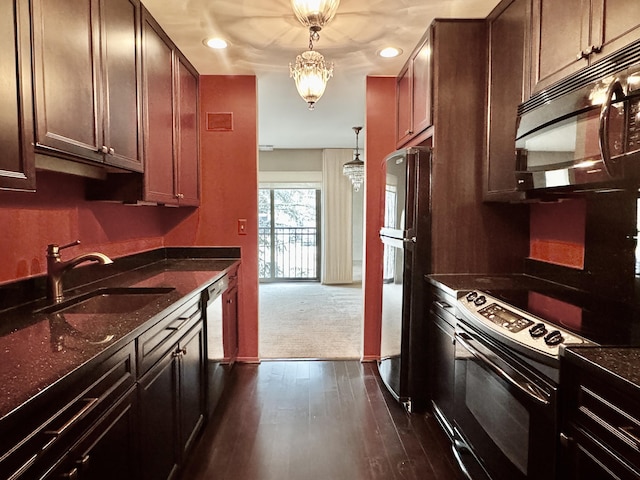 kitchen featuring sink, dark stone countertops, dark hardwood / wood-style floors, pendant lighting, and black appliances