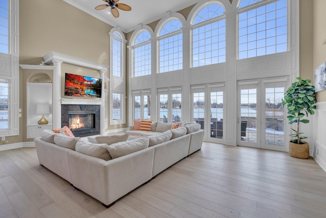 living room featuring a high ceiling, ornamental molding, ceiling fan, and light hardwood / wood-style flooring