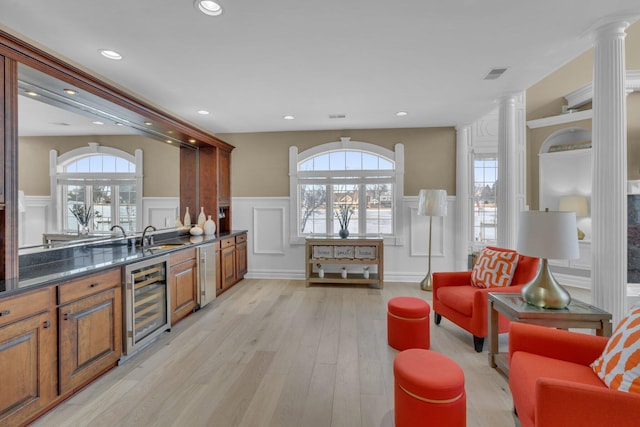 kitchen with dark stone counters, beverage cooler, light hardwood / wood-style floors, and decorative columns