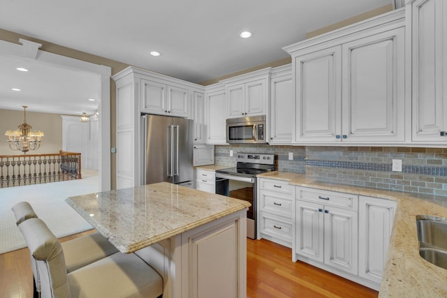 kitchen with appliances with stainless steel finishes, a breakfast bar, pendant lighting, white cabinetry, and a notable chandelier