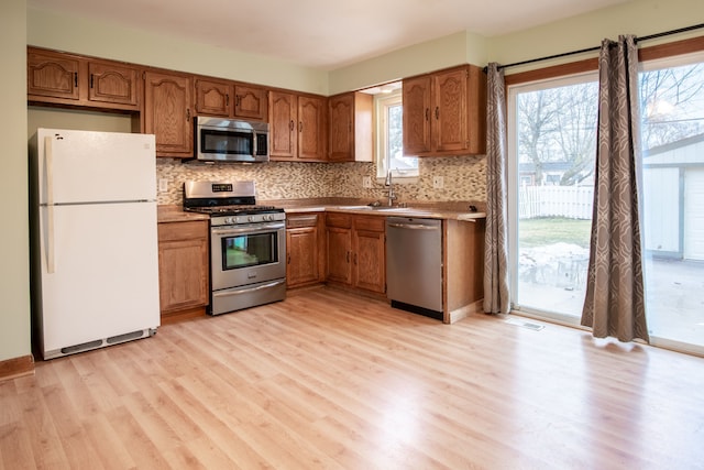 kitchen with tasteful backsplash, appliances with stainless steel finishes, sink, and light hardwood / wood-style flooring