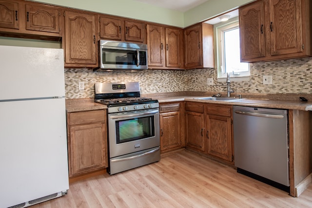 kitchen with stainless steel appliances, sink, light hardwood / wood-style flooring, and backsplash