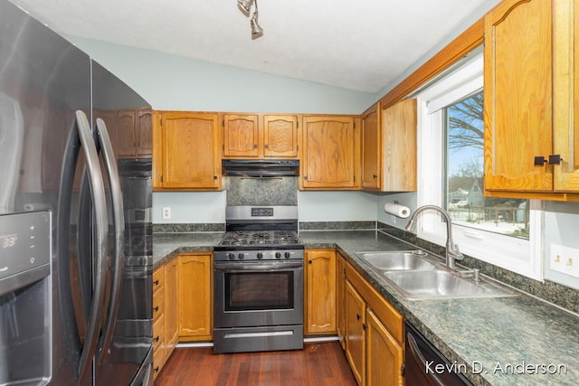 kitchen with under cabinet range hood, a sink, dark countertops, appliances with stainless steel finishes, and vaulted ceiling