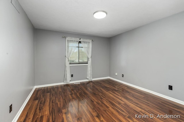 spare room featuring dark wood finished floors, visible vents, and baseboards