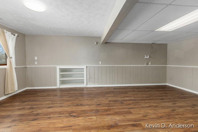 empty room featuring a drop ceiling, wainscoting, and wood finished floors