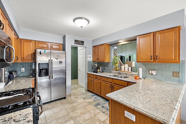 kitchen with stainless steel appliances, light stone countertops, sink, and kitchen peninsula