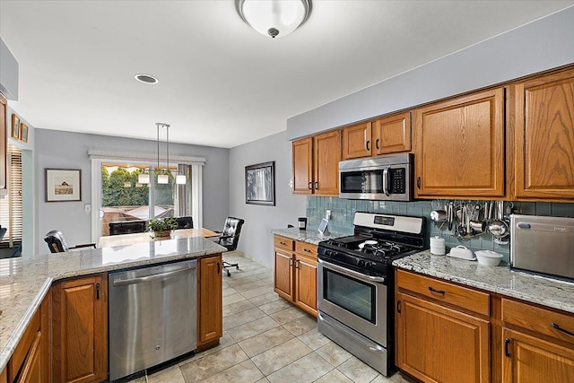 kitchen featuring light stone counters, hanging light fixtures, light tile patterned floors, stainless steel appliances, and decorative backsplash