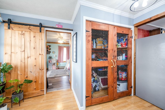 hallway featuring ornamental molding, a barn door, and light hardwood / wood-style floors