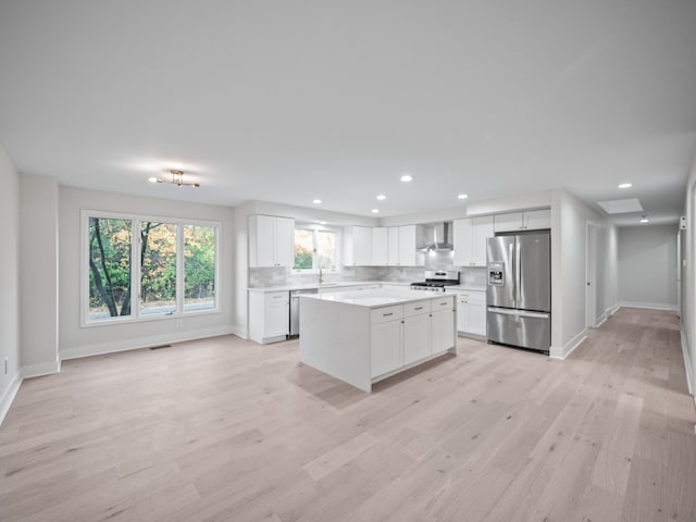 kitchen with appliances with stainless steel finishes, white cabinetry, a center island, light hardwood / wood-style floors, and wall chimney exhaust hood