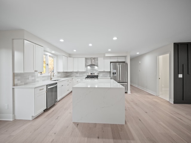 kitchen with a kitchen island, appliances with stainless steel finishes, wall chimney range hood, and white cabinets