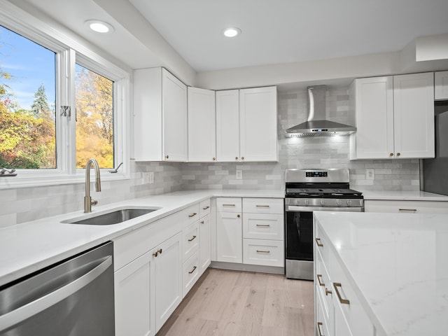 kitchen featuring wall chimney exhaust hood, sink, white cabinetry, stainless steel appliances, and light hardwood / wood-style floors