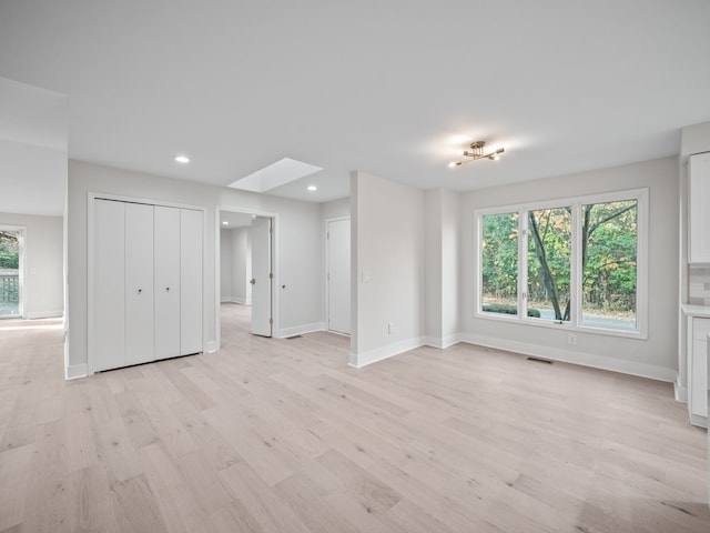 empty room with light hardwood / wood-style floors and a skylight