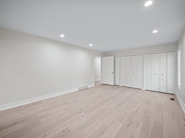 unfurnished bedroom featuring multiple closets and light wood-type flooring