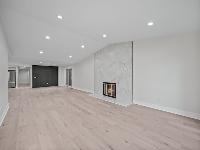 unfurnished living room featuring lofted ceiling, a high end fireplace, and light wood-type flooring