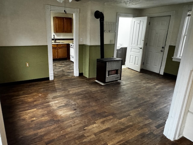 unfurnished room with sink, a wood stove, and dark wood-type flooring