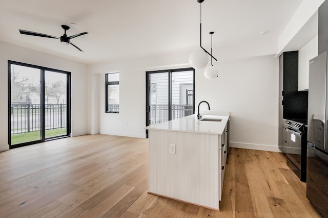 kitchen featuring an island with sink, sink, hanging light fixtures, and light hardwood / wood-style flooring