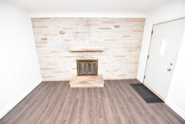 unfurnished living room with a stone fireplace, dark hardwood / wood-style floors, and brick wall