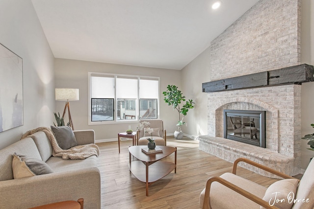 living room featuring vaulted ceiling, a brick fireplace, and light hardwood / wood-style flooring