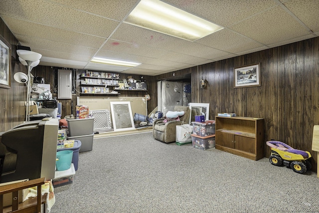 basement with carpet floors, electric panel, wooden walls, and a paneled ceiling