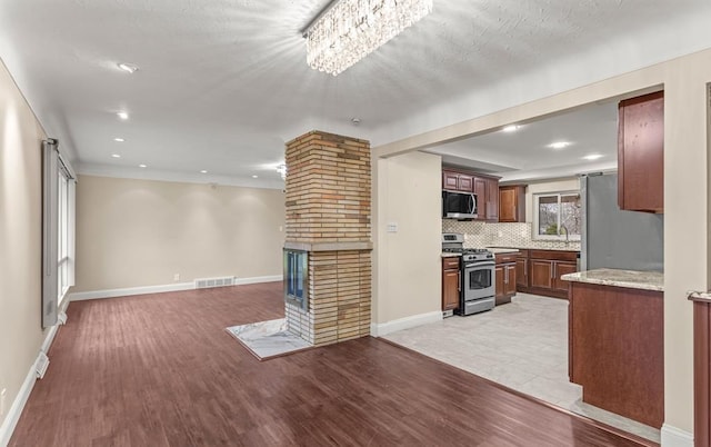 kitchen with stainless steel appliances, a fireplace, light hardwood / wood-style floors, and backsplash