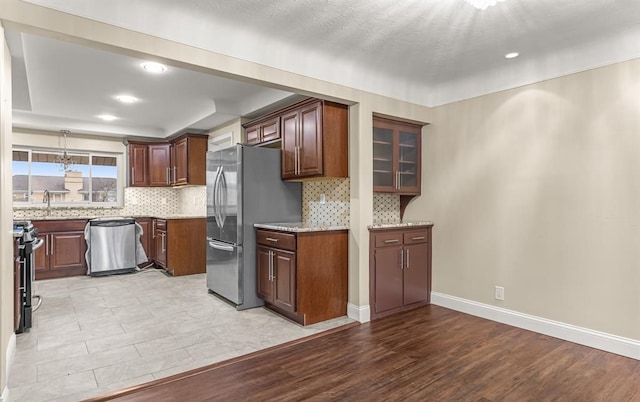 kitchen featuring light stone counters, stainless steel appliances, decorative backsplash, and light hardwood / wood-style flooring