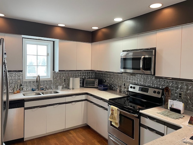 kitchen with sink, appliances with stainless steel finishes, white cabinets, hardwood / wood-style floors, and backsplash