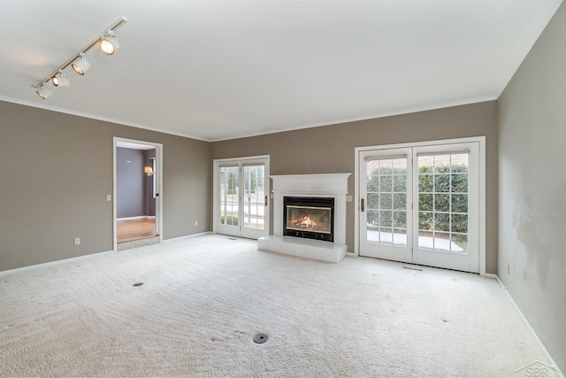 unfurnished living room with carpet floors, rail lighting, ornamental molding, a glass covered fireplace, and baseboards