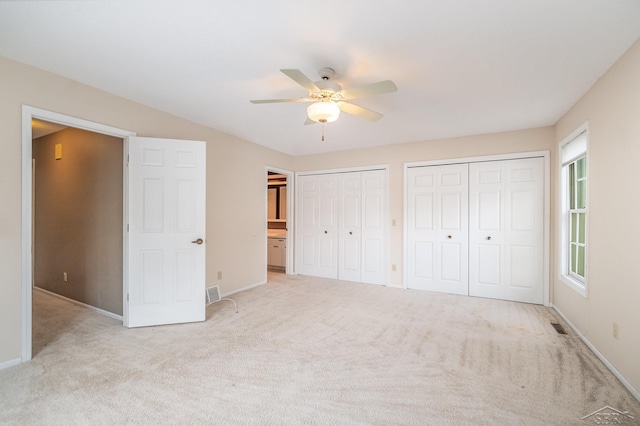 unfurnished bedroom featuring baseboards, visible vents, a ceiling fan, carpet flooring, and two closets